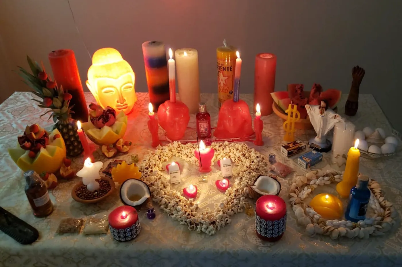 Altar com velas, coração de pipoca, frutas e búzios