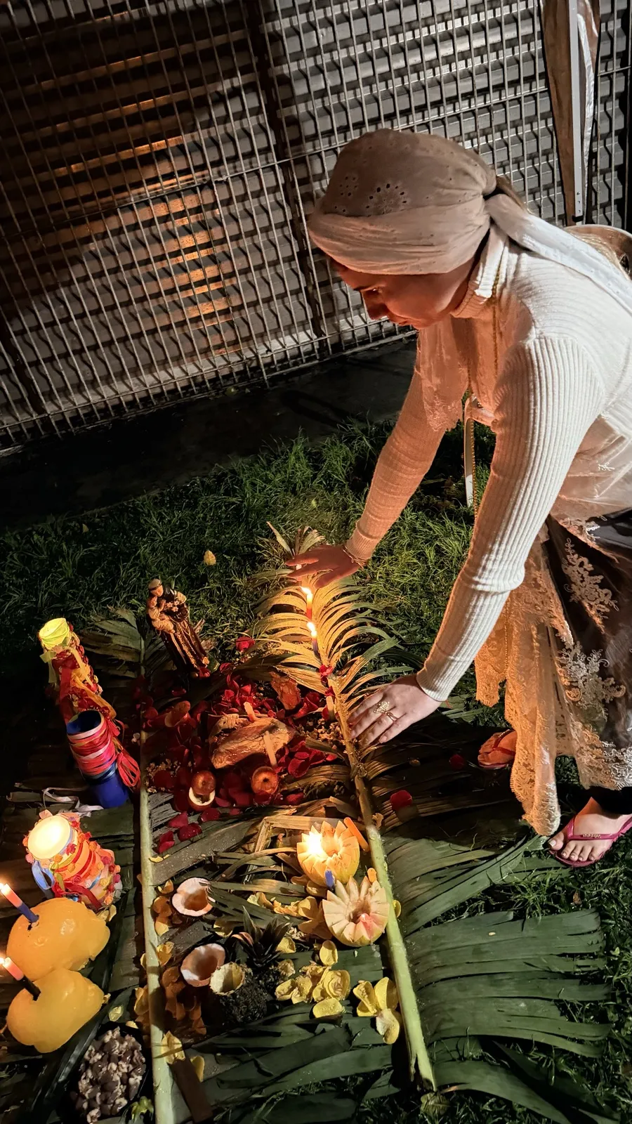 Sarah de turbante, inclinada sobre a oferenda, acendendo uma vela entre as palmas