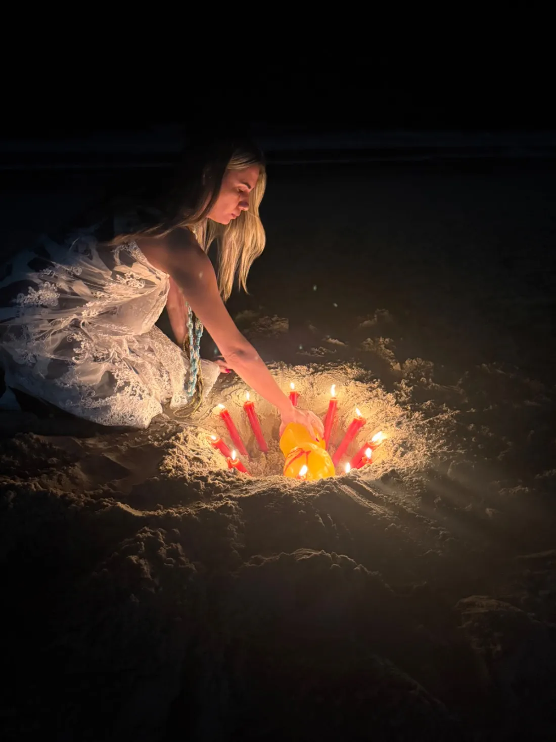 Sarah Sensitiva acendendo velas vermelhas em um círculo na areia, à noite